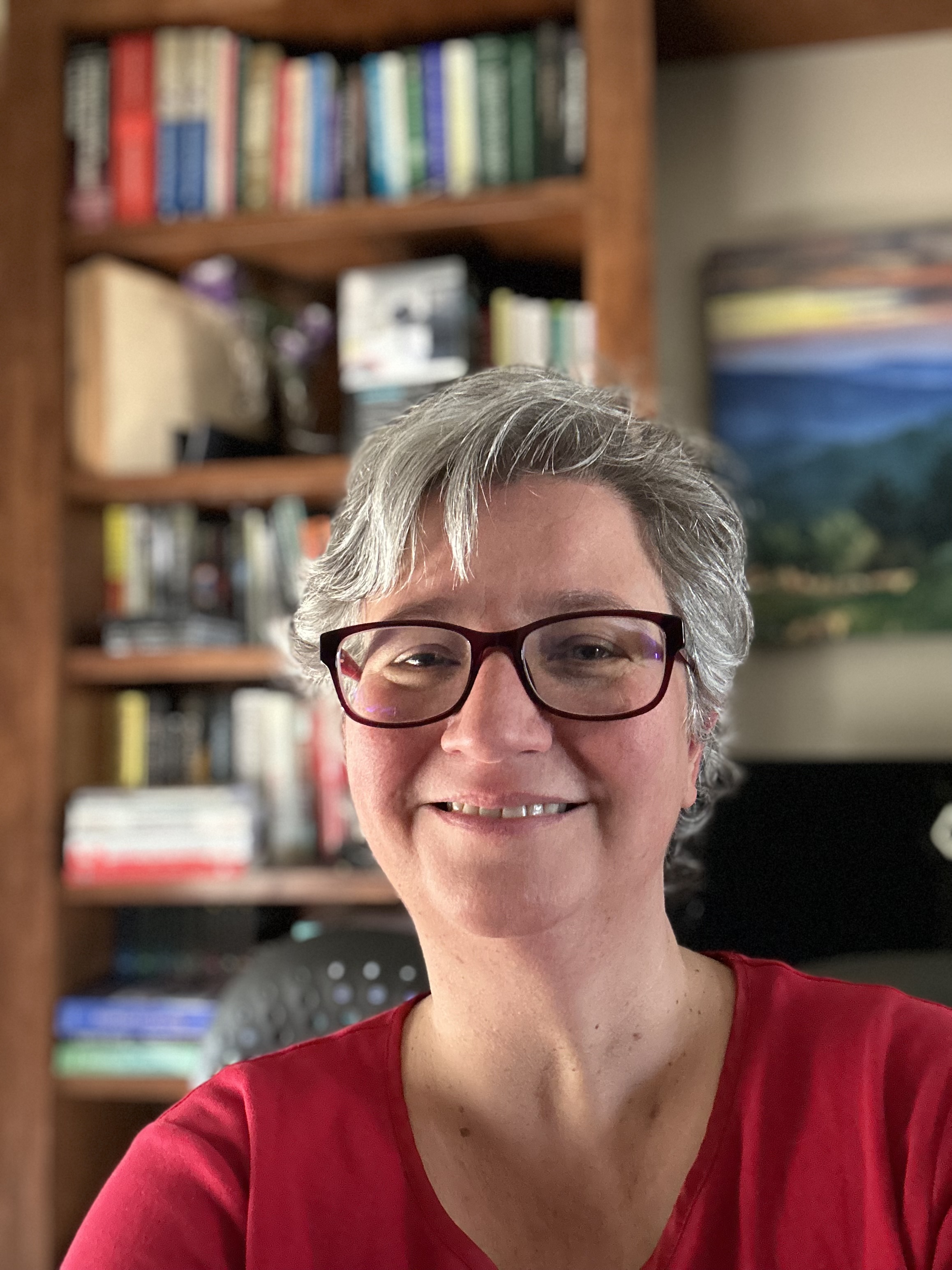 A picture of Stephanie Moore with a bookshelf in the background, who is smiling at the camera and is lit from the side.